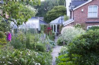 Looking down a garden path and perennial borders towards a house.