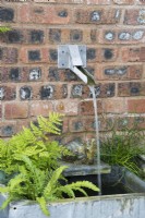 Zinc water tank water feature against red brick wall in shaded area of garden