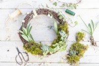 Completed wreath, moss, snowdrops, wire, string and pruning scissors laid out on a wooden surface