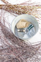 Burlap, secateurs, wire, birch sticks, pussy willow sticks and a metal basin laid out on a wooden surface