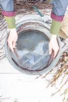 Woman placing birch sticks around the edge of the metal basin to make a homemade wreath