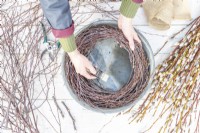 Woman wrapping wire around the birch sticks to form the homemade wreath