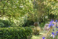 Country garden in June with a decorative metal sphere surrounded by lush planting.