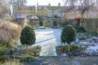 View of formal walled town garden in winter with snow covered lawn. January