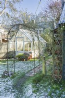 View through rose arch to traditional style painted timber greenhouse in winter. January