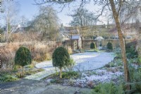 View of formal walled town garden in winter with snow covered lawn bordered by box topiary. January