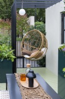 A balcony garden created as a city escape from the busy world around. An egg chair hangs from a pergola, amidst huge planters filled with foliage and flowers.