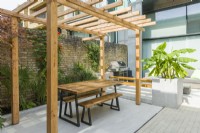 View of a contemporary courtyard garden with pergola, outdoor seating, barbeque, large planters and plants with a tropical appearance. September