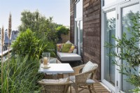 A balcony dining area is edged in planters of ornamental grasses, a standard bay, variegated pittosporum, olive and loquat.