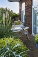 Evergreen shrubs and trees grown in planters create a leafy screen on a balcony, sheltering a dining area and day bed.