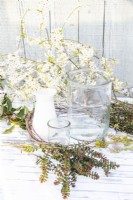Large and small glass containers, water, feathers, weeping willow, birch sticks, lichen covered twigs, hebe sprigs and blossoming blackthorn sticks laid out on a table
