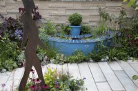 'The Lillian Prime Trust Garden' - BBC Gardener's World Live 2021 - semi circular pond painted blue, bordered by perennials in pastel shades, with hands sticking out of the water