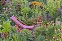 Deckchair on smal patio amongst colourful mixed border and containers.