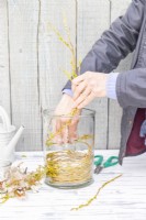 Woman placing willow twigs in the large glass container