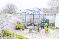 Greenhouse surrounded by potted plants in a paved garden