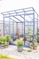 Greenhouse surrounded by potted plants in a paved garden