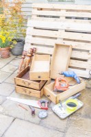 Pallets, drawers, spindles, jigsaw, drill, black paint, brush, roller, screws, saw, tape measure and pencil laid out on the ground