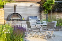 Outdoor dining area with wooden table, chairs and bespoke kitchen unit with integrated pizza oven and bbq grill. 