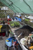 A well used greenhouse is filled with gardening paraphanlia including compost, seedlings, potting bench, tools and fitted with greenhouse shading. Spring
