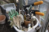 An old washing bowl makes a storage container for garden paraphernalia inside a greenhouse. The tub includes items such as scissors, shears, mallet, secateurs and gardening gloves. 