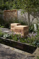The Communication Garden. Designer: Amelia Bouquet. Water rill with  wooden cubes for seating in the gravelled area and a Corylus avellana tree. RHS Hampton Court Palace Festival 2021.