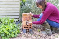 Woman filling the gaps in the bricks with dried plant stems