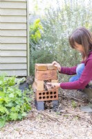 Woman filling the gaps in the bricks with dried plant stems