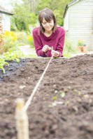 Woman tying a line to sow Salad Rocket seeds along