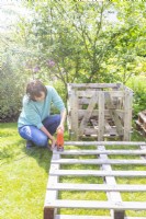 Woman sawing along the inside edge of a pallet to cut out the middle