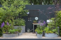 Metal containers are planted with a mix of trees such as birch, elder and apple, with herbs, purple honesty and borage.