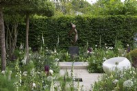 A classical, contemporary space features 'Dancers', a sculpture by Jack Eagan, offset against hornbeam hedging, amidst white and green themed borders planted with alliums, foxgloves and peonies.
