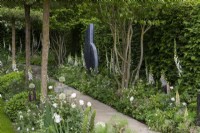 A classical, contemporary garden features flat-topped hawthorns above white and green themed borders planted with alliums, foxgloves and peonies. Sculpture 'Connected' by Tom Stogdon.