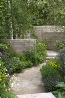 A path edged in birch trees, valerian, euphorbia, hardy geraniums and verbena leads to a series of clay-rendered, sculptural walls that swirl through the sloping garden.