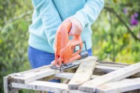 Woman sawing to remove the middle of one of the sides of the pallet crate
