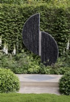 Contemporary Slate and steel garden sculpture set against hornbeam hedge 