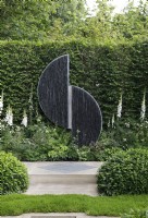 A sculpture of steel and slate, titled 'Connected' by Tom Stogdon creates a focal point in The Perennial Garden 'With Love', it is surrounded by digitalis purpurea f. albiflora, the lawn at the front is a chamomile lawn - Designer: Richard Miers - Sponsor: Perennial