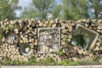 Insects hotels made in wall of stacked tree trunks and concrete drainage pipes. 