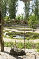 View over The Spiral of Life garden at a garden show with water chain and circular paths over pond with pond planting.