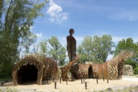 Arches of willow branches and corten steel human statue as landart designed by Will Beckers.