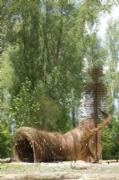 Arch of willow branches and corten steel human statue as landart designed by Will Beckers.