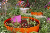 Orange metal raised ponds with water plants, pink inset container with Iris sibirica - The St Mungo's Putting Down Roots Garden, RHS Chelsea Flower Show 2022 - Silver Medal