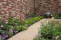 Border next to a clay paver path with Paeonia 'Coral Sunset',  Rose 'Queen of Sweden', Tiarella 'Pink Skyrocket' and Hakonechloa macra - The Stitcher's Garden, RHS Chelsea Flower Show 2022 - Silver Medal