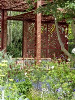 Ornamental metal trellis work in show garden setting with soft summer planting and seating area.