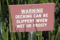 A red sign warning public of potentially slippery decking when wet or frosty
