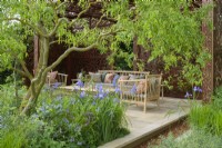 Sitting arrangement in pavilion  of metal screens  with  Morris' Willow Boughs pattern also on cushions, surrounded by herbaceous beds with blue Iris siberica sp and  Salix matsudana tortuosa tree, dragon's claw willow  