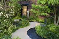 Curved path leading to doorway and rill around  bed planted with Cornus kousa var. chinensis above shade-loving hostas, primulas, irises and disporum - The Boodles Travel Garden