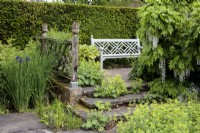 An ornate wooden garden bench in the Lower Rill Garden at Wollerton Old Hall Garden, with Iris siberica, and  Alchemilla mollis, Ladies Mantle.