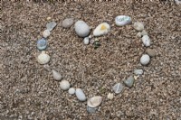 A heart made of pebbles, stones and painted rocks decorates a gravel area. Briar Cottage Garden. Devon NGS garden. Spring
