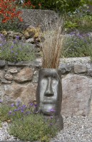 Easter Island style sculptural head planted with ornamental grass to add interest to terracing. Spring