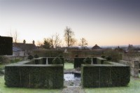 Yew hedges frame a circular pond in a formal town garden in winter